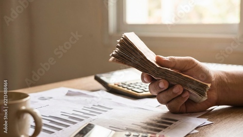 Hand counting cash banknotes over financial charts on desk for budgeting, personal finance and household savings
