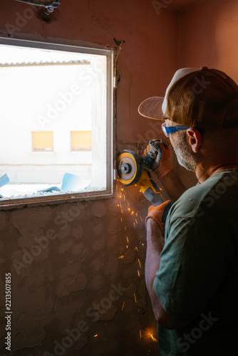 Manual worker using angle grinder on window frame in home renovation