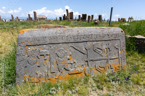 Inscribed khachkar stone standing among countless weathered stelae forming a dense ancient stone forest with Armenian script at Noratus medieval cemetery, Noratus, Armenia