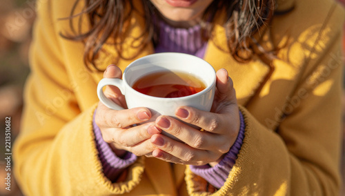 Woman holding a warm cup of tea outdoors in sunlight.