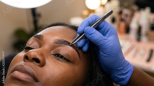 Beautician Shaping Eyebrows with Tweezers on Woman's Face