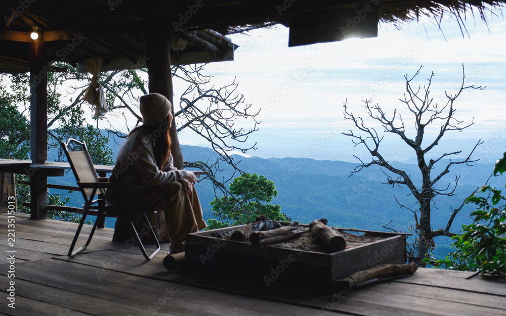 Fototapeta premium Rear view of a woman sitting on wooden terrace and looking at nature views