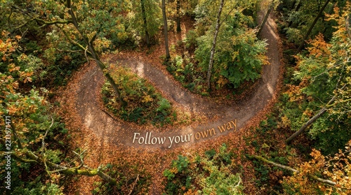 Aerial view of a winding forest path covered in autumn leaves, with text 'Follow your own way'