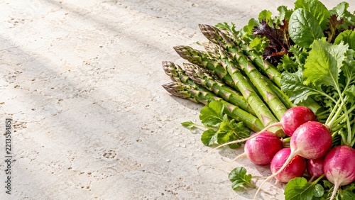 Fresh Asparagus and Radishes with Water Droplets on a Cream Stone Table