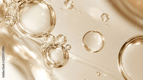 透明な美容液バブルの集まりと流れるジェルが輝く高級保湿スキンケア背景 / Clustered clear serum bubbles and flowing gel in warm gold tones for premium hydrating skincare backgrounds