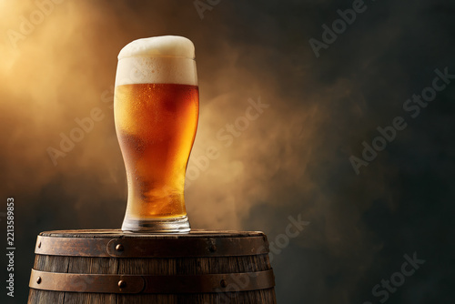 Beer glass with foam on wooden barrel against smoky amber background, Oktoberfest product shot