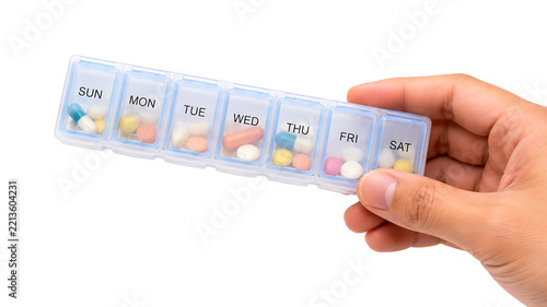 Hand holding weekly pill organizer with colorful medicine capsules on white background