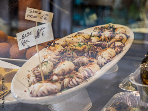 Fotografie VENICE, ITALY - APRIL 6, 2016: Grilled cuttlefish with parsley displayed for sale at an Italian seafood counter with a handwritten price sign