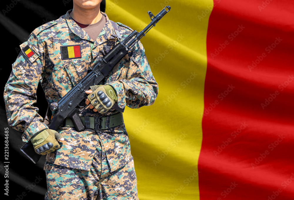 Fototapeta premium Belgium flag with soldier in military uniform holding assault rifle in front of it
