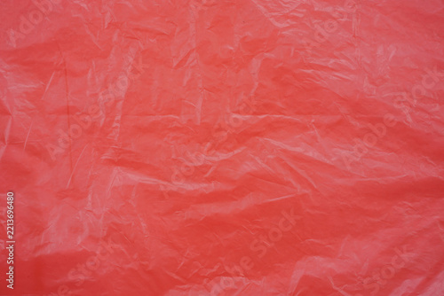 Red crumpled plastic texture with irregular wrinkles and folds, creating an abstract textured background with natural highlights and shadows