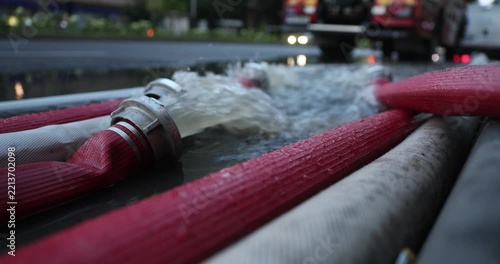 Water coming out of high-pressure red and white fire hoses along a city street during emergency flooding operations