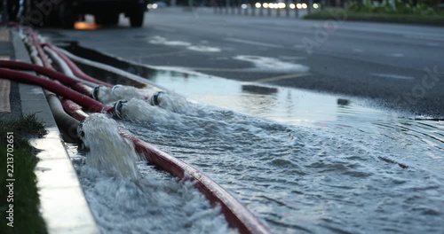 Water coming out of high-pressure red and white fire hoses along a city street during emergency flooding operations