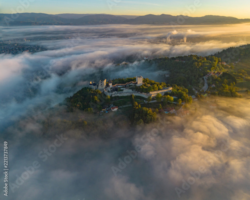 Fotografie Aerial drone view of the medieval Celje Castle surrounded by morning fog and golden sunrise light in Slovenia