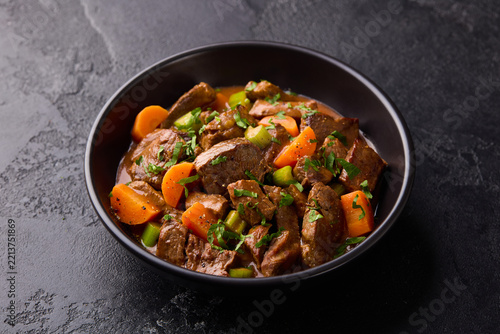 Beef stew with carrots and celery in a black bowl. Slate background. Close up.