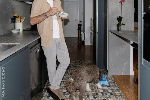 Anonymous senior man eating in kitchen beside Spanish water dog