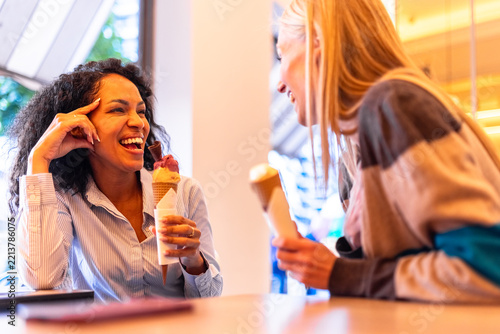Two happy women enjoying ice cream cones, sharing a moment of laughter and friendship at a cafe during summer, embracing joy and connection