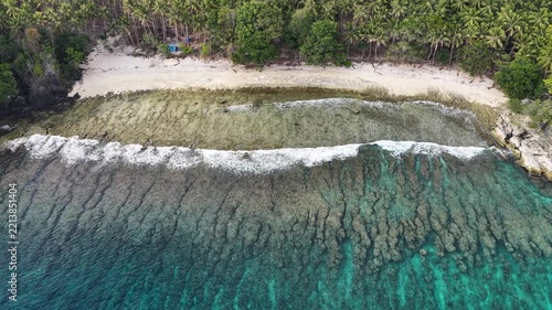 Calm seas bathe the beautiful coastline of the remote Maju Island in the Molucca Sea, Indonesia. A rugged, rocky reef surrounds this tropical paradise which few people ever visit.