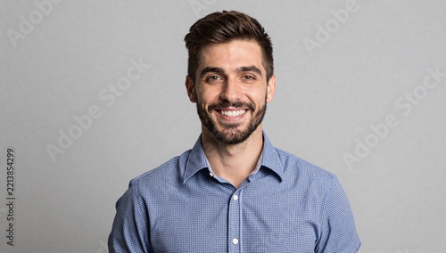 Smiling man with short brown hair and beard wearing a blue patterned shirt against a gray background