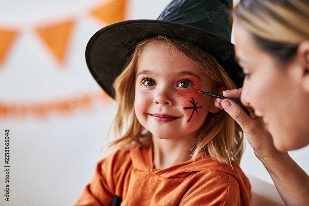 Fototapeta premium Child in witch costume getting Halloween face paint by makeup artist