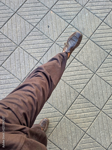 Legs of a man in a brown leather shoes on the pavement