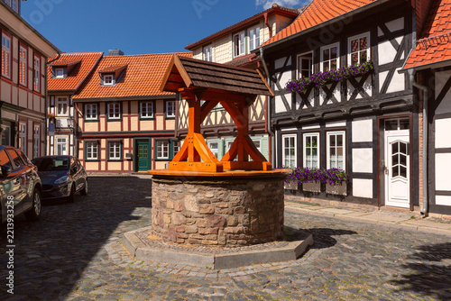 Picturesque cobblestone street with traditional half-timbered houses, colorful flowers and an old stone well in Wernigerode, Germany.