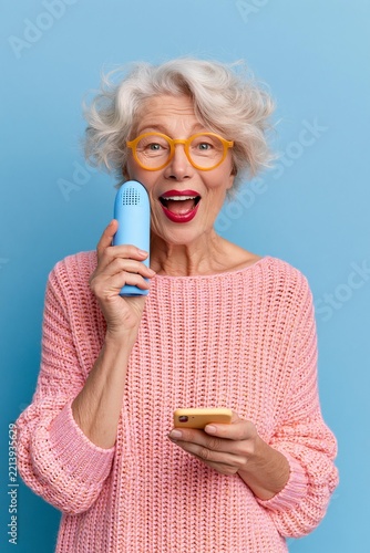 Voice app. Cheerful excited elderly woman grandmother hold smartphone by mouth dictate request to virtual assistant record vocal message. Happy aged lady use phone loudspeaker for easy communication