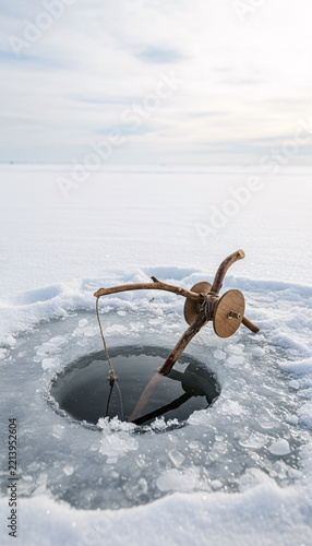 An ice fishing hole with a wooden rod, simple, rustic and handmade, bright airy daylight