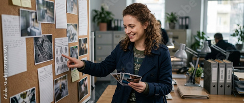Smiling Woman Detective Examining Evidence Board with Photos and Notes