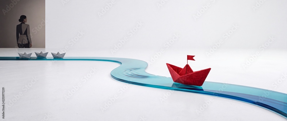 Fototapeta premium Concept of Leadership and Visionary Direction Featuring a Red Paper Boat with a Flag Leading Grey Boats Along a Winding Blue Path with a Businesswoman Watching in a Minimalist Studio Environment