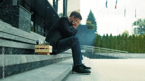 Unemployed businessman covering face on building steps in disbelief. Corporate collapse crisis