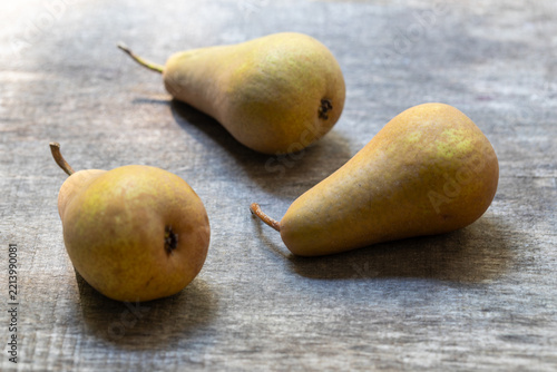 Three ripe pears on a rustic wooden table in natural side light