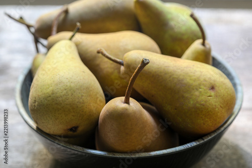 Ripe green and yellow pears in a dark rustic bowl, close-up