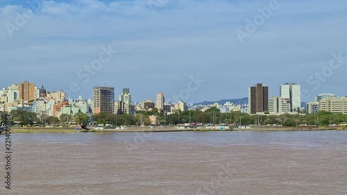 Wide panoramic view across the broad river toward the downtown skyline and waterfront park of Porto Alegre Brazil under a clear light blue sky on a bright sunny day