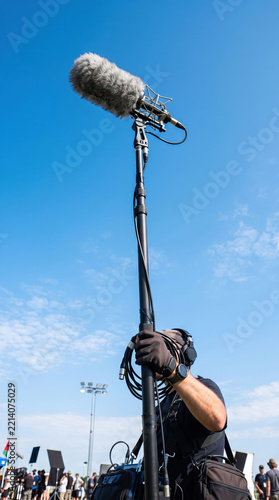 Overhead boom microphone against blue sky captures outdoor sound recording at public event
