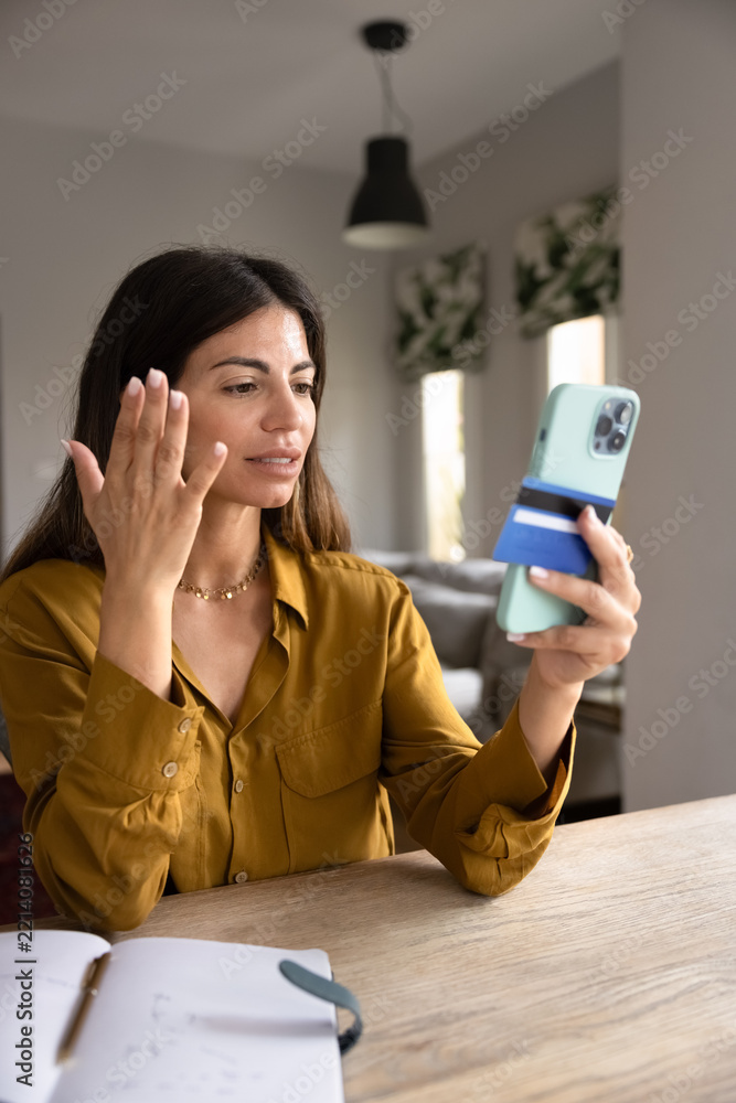Fototapeta premium Woman holding smartphone and card feeling stressed due to declined credit card, insufficient funds in bank account, unexpected charges. Financial concerns, payment failure, or failed money transfer