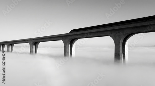 cinematic train journey through mist concept. Elevated bridge pierces through thick fog in a monochrome landscape.