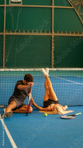 A young couple resting on a blue indoor tennis court after a long and intense practice session