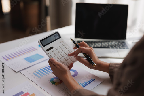Businesswoman calculating finances using a calculator, analyzing financial reports with charts and data in an office