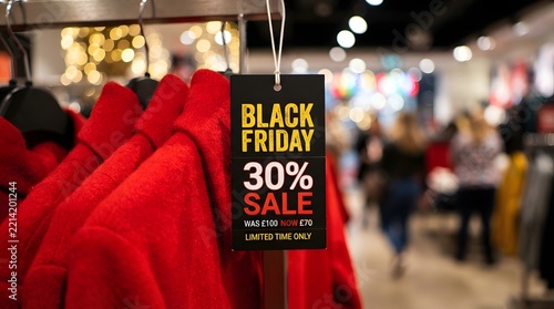 Black friday sale tag hanging on a rack of red coats in a clothing store with a 30% discount from 100 to 70 for limited time holiday shopping