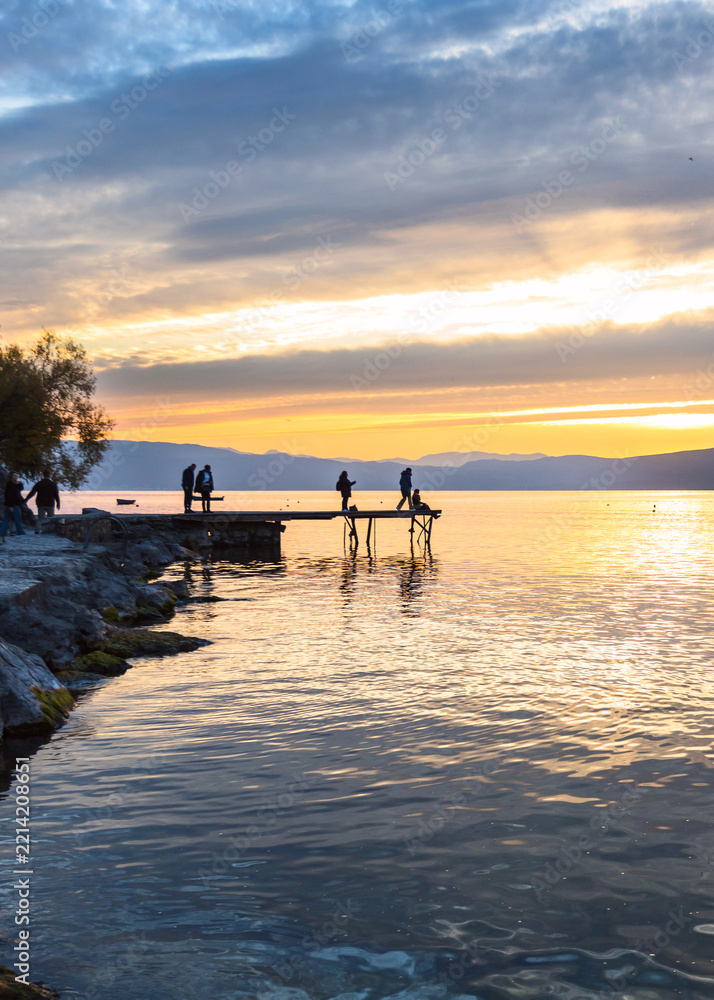 Fototapeta premium People walking on a lakeside pier at sunset
