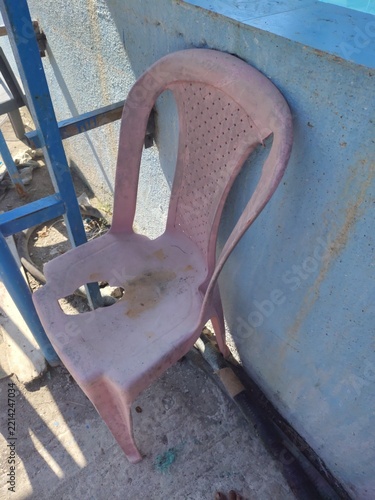 Broken plastic chair standing on a weathered concrete floor near a blue wall with damaged furniture worn out old furniture outdoor seating rough texture damaged seat worn down