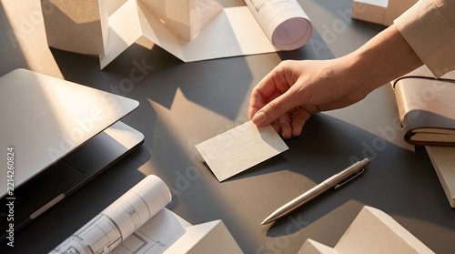 Professional hands organize business cards and architectural models on a sleek modern office desk during sunset.
