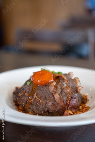 Beef fat fried rice topped with sliced medium rare picanha steak and a pickled egg yolk on a plate.