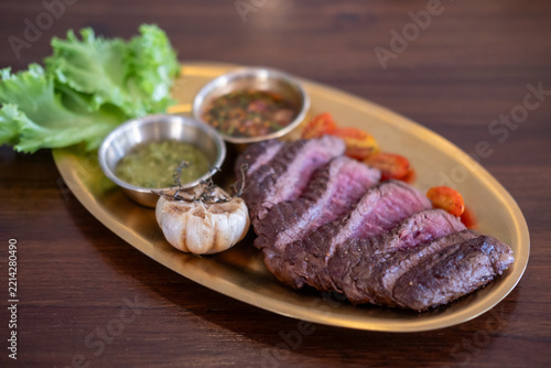 Sliced medium rare tenderloin steak served on a plate with whole cloves of roasted garlic.