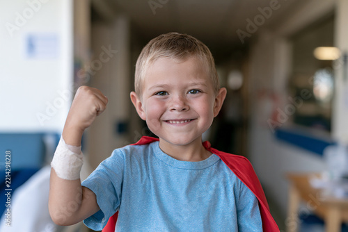 Happy child wearing medical wristband and superhero cape in pediatric hospital, playful confident pose, childhood cancer awareness, courage, strength and positive coping concept.