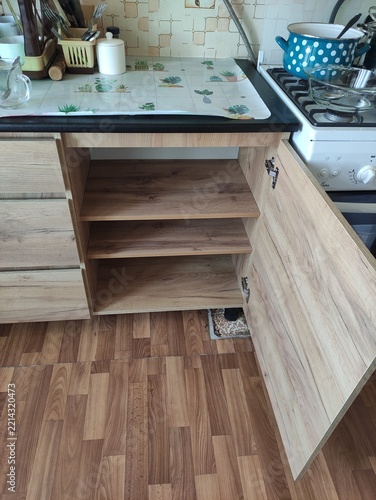 Open wooden kitchen cabinet with empty shelves under a countertop in a kitchen