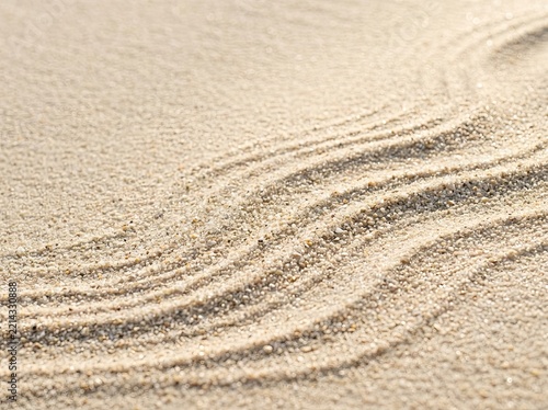 Close-up view of textured sand on a beach with curved patterns formed by wind or raking, illuminated by soft golden hour sunlight.