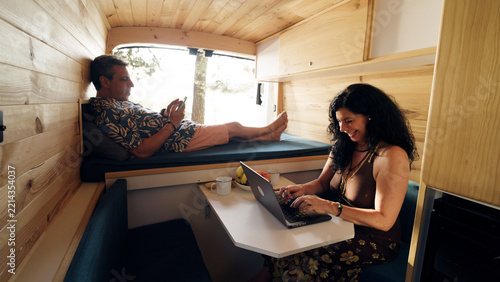 Couple working remotely and relaxing inside a modern wooden camper van, living the freedom of travel and remote work