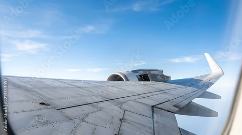 Passenger jet airplane wing and engine flying through clear blue sky viewed from window seat