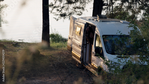 Mature couple relaxing inside a camper van parked by a serene lake, embracing freedom and travel lifestyle in nature